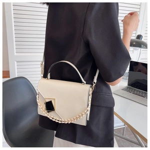 Detail of a creamy white handbag with a geometric clasp and metal chain on a model
