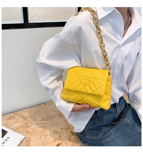 Detail of yellow quilted flap bag with chunky gold chain strap worn with a white shirt