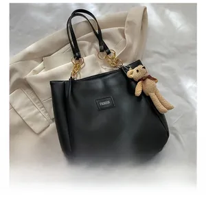 Detail of black leather tote bag with gold chain strap and cute teddy bear pendant