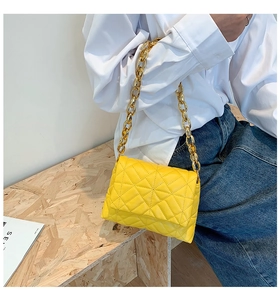Detail of yellow quilted leather handbag featuring a bold gold acrylic chain strap