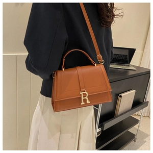 Detail of a brown leather shoulder bag with gold R hardware worn by a model in a modern office