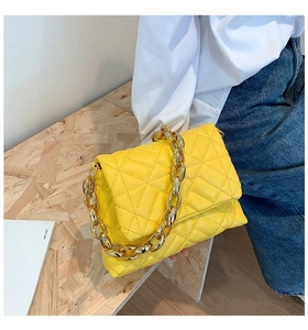 Detail of yellow quilted shoulder bag with bold gold acrylic chain on wood texture