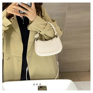 Close-up of a white textured leather half-moon bag featuring a metal chain strap and top handle