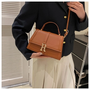 Detail of caramel brown handbag with matte leather texture and gold R-shaped metal buckle