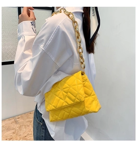 Detail of yellow quilted flap bag featuring a bold chunky gold acrylic chain strap