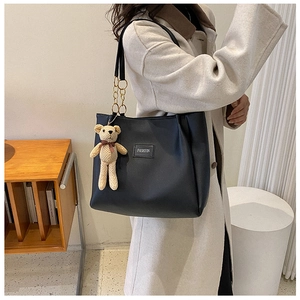Detail of black leather tote bag with metal chain strap and cute bear charm pendant
