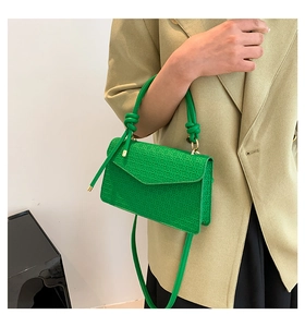 Detail of green woven crossbody bag with knotted handle and textured envelope flap
