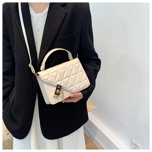 Detail of cream-white quilted crossbody bag with black buckle and gold chain strap