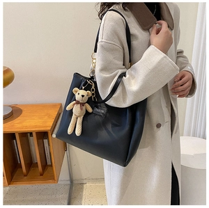 Dettaglio borsa tote in pelle nera con ciondolo a forma di orsetto e etichetta moda