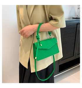 Detail of green embossed crossbody bag with knot handle and gold hardware on model