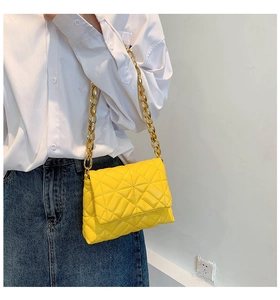Detailed shot of yellow quilted shoulder bag featuring chunky gold acrylic chain link strap