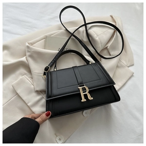 Close-up of black crossbody bag with golden R-letter buckle on stylish blazer background