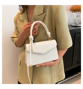 Close-up of white embossed leather handbag with gold hardware and top handle detail