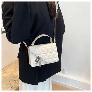 Detail of white quilted crossbody bag featuring gold chain lock and stylish triangular pattern