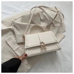 Detailed view of white square handbag featuring gold R-logo metal buckle and smooth faux leather