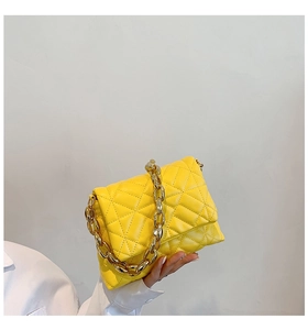 Detail of a bright yellow quilted shoulder bag with a bold gold acrylic chain handle