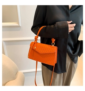 Detail of orange woven textured handbag with knot handle and gold hardware on model
