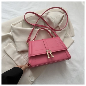 Close-up of fuchsia crossbody bag with golden R-letter buckle on a white blazer