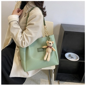 Detail of light green tote bag with gold chain and knit bear charm on model