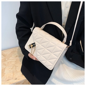 Detail of white quilted handbag featuring a gold-toned twist lock and chain decoration