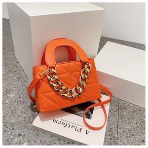 Detail of bright orange quilted PU handbag featuring bold gold chain and top handle