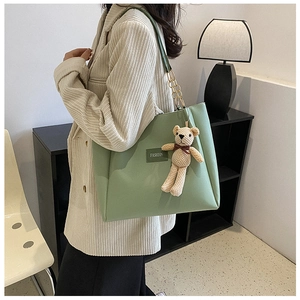Dettaglio della borsa tote verde chiaro con tracolla a catena e ciondolo a orsetto