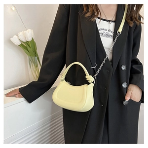 Detail of a creamy yellow semi-circular handbag with knot accents and chain strap