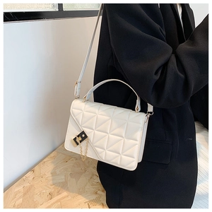 Detail of white quilted crossbody bag with gold lock shown on black blazer suit