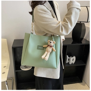 Dettaglio della borsa tote verde chiaro con catena dorata e ciondolo a orsetto