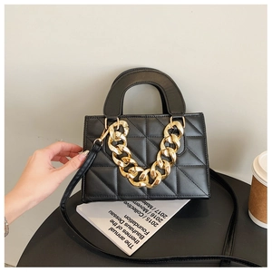 Detail of black quilted leather handbag featuring a bold gold chain and crossbody strap