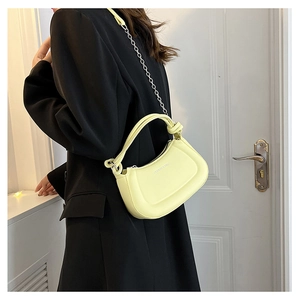 Detail of yellow crescent bag featuring a knotted handle and metallic chain strap