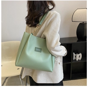 Detail of light green leather tote bag with gold chain strap worn by a model