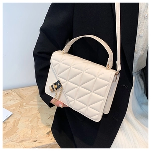 Close-up of a white quilted crossbody bag with gold chain charm on a black blazer