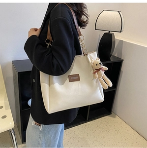 Detail view of beige tote bag featuring chain straps and a cute knitted bear charm