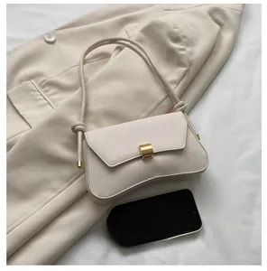 Detail of minimalist cream leather crossbody bag with square gold lock and phone for scale