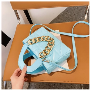 Detail of light blue quilted handbag with chunky gold chain on a leather chair