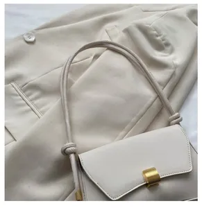 Detail of minimalist cream square bag featuring a brushed gold metal clasp and knotted strap