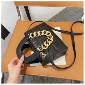 Close-up of black quilted handbag with chunky gold chain handle on leather chair