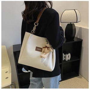 Dettaglio della borsa tote crema con spalline in pelle marrone e ciondolo a orsetto