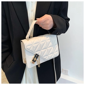 Detail of white quilted handbag with metal chain and lock held by a model in black blazer
