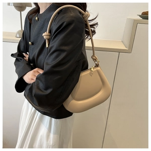 Detail of beige underarm bag with knotted shoulder strap and gold zipper on a model