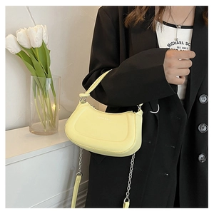 Detail of light yellow crescent shoulder bag with silver chain strap on black suit