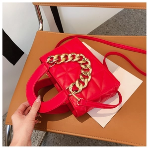 Detail of red quilted faux leather handbag with chunky gold chain on brown leather chair