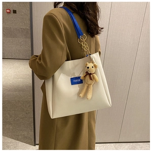 Dettaglio borsa tote color crema con tracolla blu, catena oro e orsetto morbido
