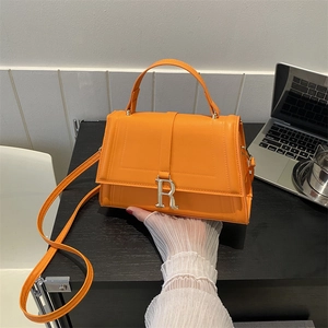 Chic orange faux leather crossbody bag with silver R-buckle and top handle on black surface