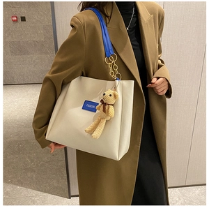 Dettaglio della borsa tote bianco sporco con tracolla blu e ciondolo orsetto giallo