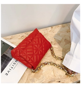 Detail of red quilted PU leather bag with chunky gold chain on a wooden surface