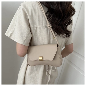 Detail view of beige leather underarm bag with golden buckle on a model shoulder