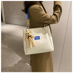 Dettaglio della borsa tote bianco off-white con tracolla blu cobalto e ciondolo a orso