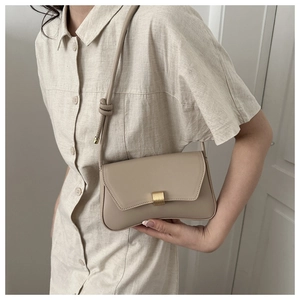 Close-up of minimalist beige crossbody bag with matte gold buckle and knotted strap detail
